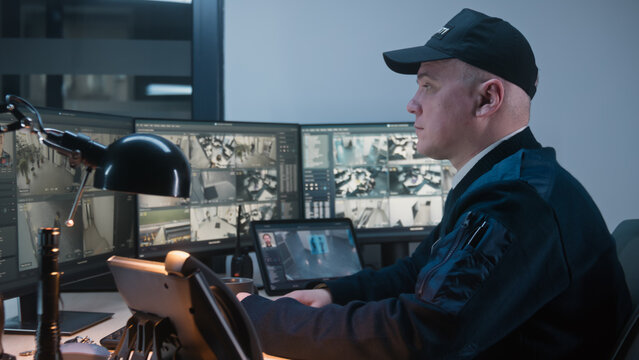 Security officer controls CCTV cameras in office, uses digital tablet and computers, makes call by landline phone. Software showing surveillance cameras footage on screens. Concept of social safety.