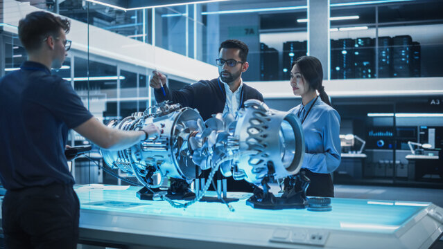 Young Team of Multicultural Engineers Use Blueprints, Tablet and Laptop Computers, Analyze and Discuss How a Modern Electric Turbine Motor Works. High Tech Research Laboratory with Modern Equipment.