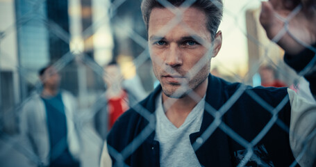 Portrait of a Handsome Caucasian Man Holding the Fence, Posing and Looking at Camera while Standing Outdoors in an Urban City Location. Stylish Diverse Friends Standing Behind Him