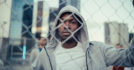 Portrait of a Handsome African American Man Holding the Fence, Posing and Looking at Camera while Standing Outdoors in an Urban City Location. Stylish Diverse Friends Standing Behind Him