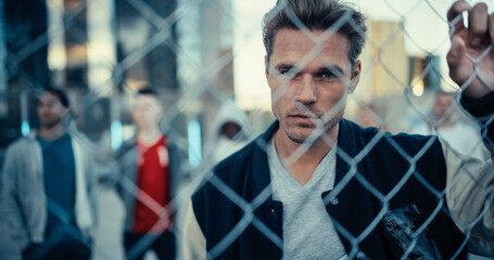 Portrait of a Handsome Caucasian Man Holding the Fence, Posing and Looking at Camera while Standing Outdoors in an Urban City Location. Stylish Diverse Friends Standing Behind Him