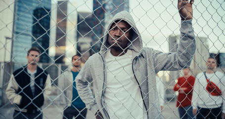Portrait of a Handsome African American Man Holding the Fence, Posing and Looking at Camera while Standing Outdoors in an Urban City Location. Stylish Diverse Friends Standing Behind Him