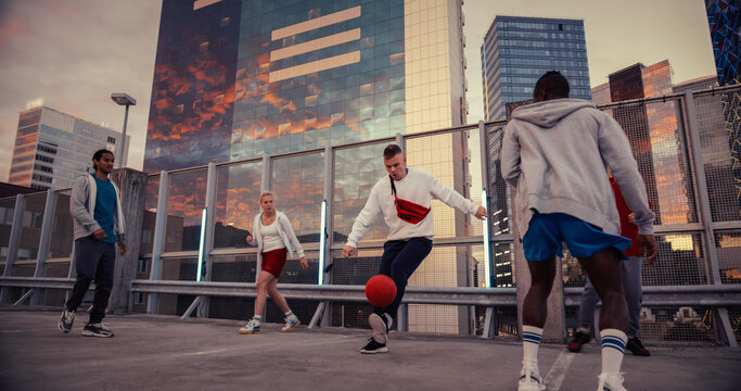 Young Man Playing Soccer with Diverse Friends. Multiethnic Stylish Group Enjoying a Game of Football at an Urban Parking Lot on Rooftop with Skyscrapers at Sunset. African Player Scoring a Goal - Powered by Adobe