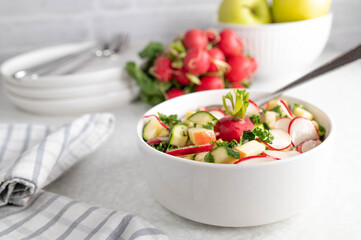 Cucumber, apple, red radish salad marinated with honey, olive oil, lemon juice and parsley. Served ready to eat in bowl with fork on white table background