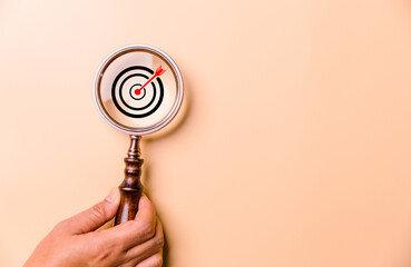 Hand holding target board inside vintage magnifying glass for focus business objective on orange...