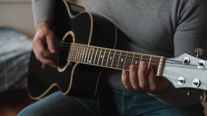 Playing the guitar. Strumming acoustic guitar. Musician plays music. Man fingers holding mediator. Man hand playing guitar neck in dark room. Unrecognizable person rehearsing, fretboard close-up