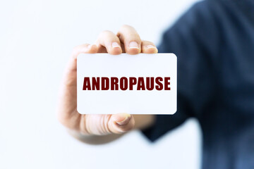 Andropause text on blank business card being held by a woman's hand with blurred background. Business concept about andropause.