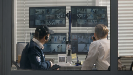 Security officers sit in surveillance room and look on security cameras view displayed on computer...