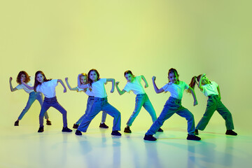 Artistic, talented little girls, children in casual sporty clothes dancing hip-hop against green studio background in neon light. Concept of childhood, hobby, sportive lifestyle, friendship, education