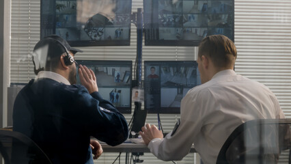 Security officers sit in surveillance room and monitor CCTV cameras with AI scanning system on computer screens using modern software. Security guard uses radio set. Concept of observation and safety.