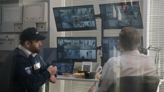 Two security operators have lunch while monitor CCTV cameras on computers. Software with footage of surveillance cameras with facial recognition on screens. High tech security. Social safety concept.