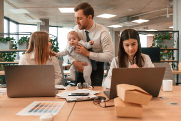 Father is holding his son. Infant baby is in the office where group of people are working together