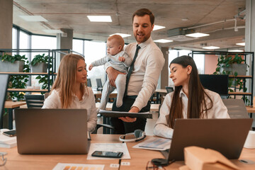 Infant baby is in the office where group of people are working together