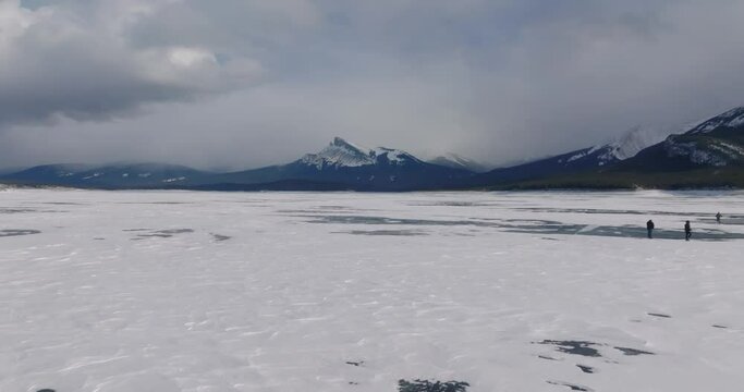 flying above ice of frozen abraham lake with rocky mountains on background in canada