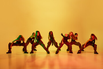 Contemp dance, hip-hop. Group of little girls, children, in stylish sportive clothes dancing against yellow studio background in neon light. Concept of childhood, hobby, sportive lifestyle