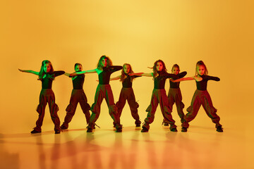 Group of little girls, children, talented dancers in stylish sportive clothes dancing against yellow studio background in neon light. Concept of childhood, hobby, sportive lifestyle, dance class