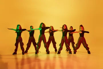 Poster Dance School Group of little girls, children, talented dancers in stylish sportive clothes dancing against yellow studio background in neon light. Concept of childhood, hobby, sportive lifestyle, dance class