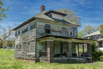 Old abandoned two story wooden home with large front porch left to rot on sunny day - 593952023