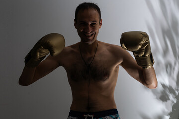 closeup shot of young naked boxer wearing protecting gloves. throwing puches in a boxing ring. grey background © Angelov