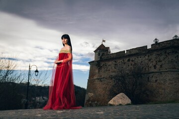 Woman wearing a medieval red dress posing against ancient buildings