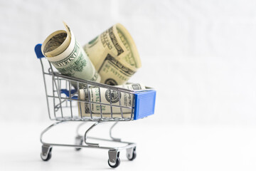 A small shopping cart with 100 dollar bills on a table with space for text.