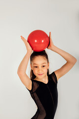A girl gymnast in a black leotard with a red ball on a white background, close-up portrait. Front...