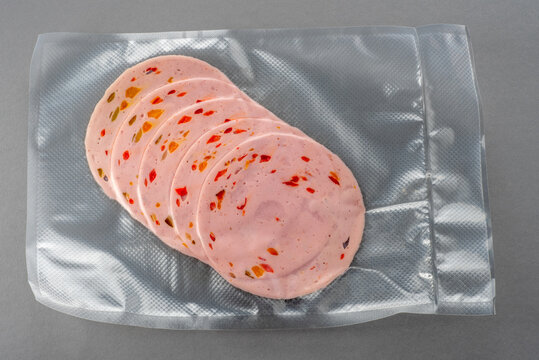 Paprika lyoner sausage slices with bell pepper in vacuum sealed package for sous vide cooking on gray background