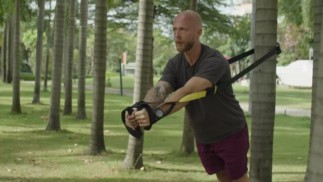 Full shot of strong man doing chest flys on suspension straps during outdoor workout in park