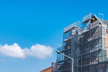 Scaffolding covered with mesh near a building being restored against a blue sky.
