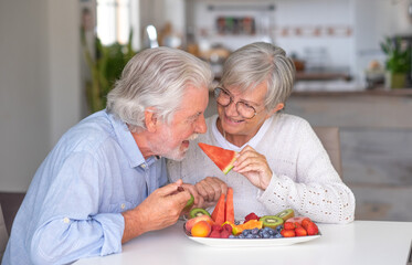 Cheerful senior couple at home having breakfast together with fresh seasonal fruit, healthy eating concept