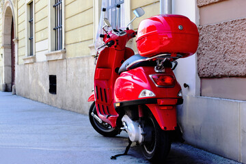 stylish red italian scooter. bright red vintage moped with storage box. old urban historic city setting. light gray cobblestone pavement.  tourism, travel and vacationing concept. stucco exterior wall
