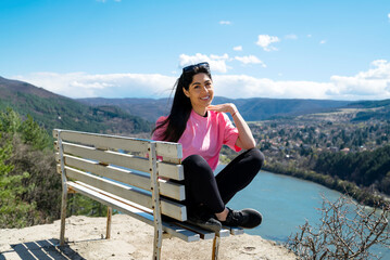 Traveler woman sitting on a bench high above a blue lake with stunning view . Scenic landscape from Bulgaria