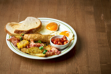 English breakfast with sausages, scrambled eggs, beans and toast in a plate on a wooden background