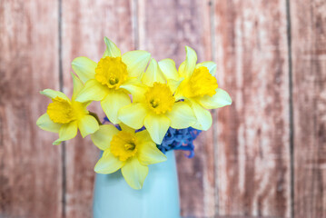 Yellow narcissus flowers bouquet in vase on wooden background 