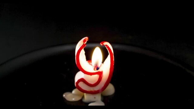 Vela de cera con forma del n&uacute;mero 9 consumi&eacute;ndose a c&aacute;mara r&aacute;pida en fondo negro
