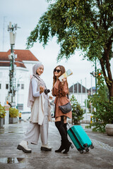 two beautiful travellers walking together through the sidewalk and showing their travel equipment