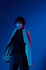Man in fashion coat on dark blue background, neon light, style and trends, mixed light, men's fashion