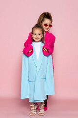 Two little girls dressed like adults. Children wearing oversized clothes. fashionable kids. Isolated on pink background.