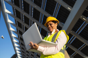 Black woman using laptop on construction site with solar batteries