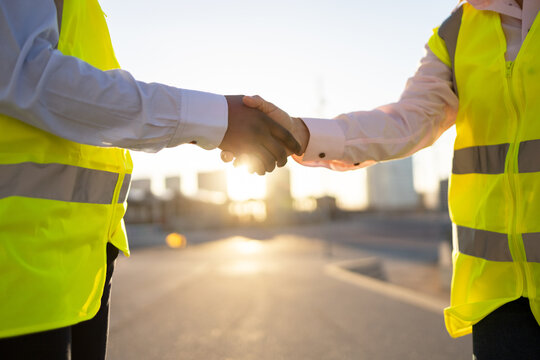 Crop engineers in site waistcoats shaking hands on street