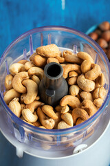 Cashews in the food in the food processor.  Cashews in blender on a blue wooden table.