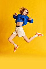 Fototapeta na wymiar Studio shot with young, gorgeous red haired girl jumping and smiling over yellow studio background. Feel of freedom