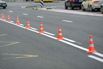 Road surface marking and traffic cone on asphalt road. Orange pylon stands on new marking on the road. Road line painting, paint white marking on asphalt surface..