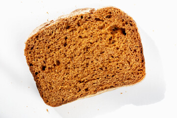 Slice of fresh delicious dark bread on white background in sunlight