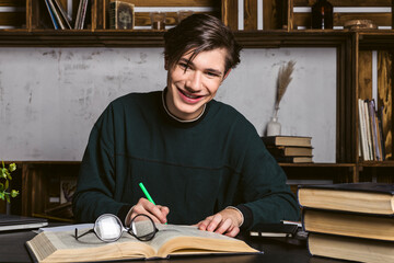 Fototapeta na wymiar A studious young man dressed neatly, in round glasses, sitting at the desk, learning and reading books.