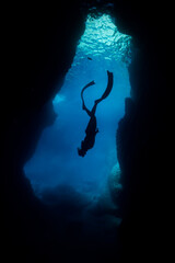 silhouette of diver woman freediving in cave.