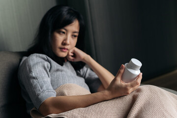 Asian woman with cold and flu reading instructions on medicine bottle