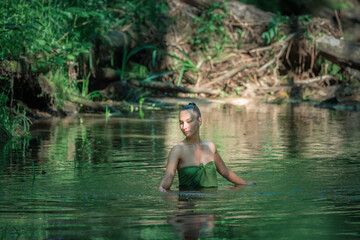 Young beautiful dark-haired girl posing in a forest river.