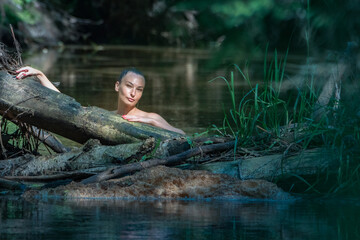 Young beautiful dark-haired girl posing in a forest river.