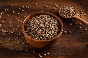 Uncooked coriander seeds bowl. Studio shoot isolated on rustic background. Coriander seeds spread on dark background. 45 degree shoot.